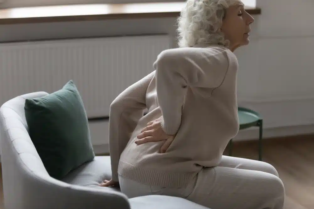 Unhealthy,Older,Woman,Stand,Up,From,Chair,Touch,Back,Suffer Woman experiencing low back pain when transitioning from sitting to standing