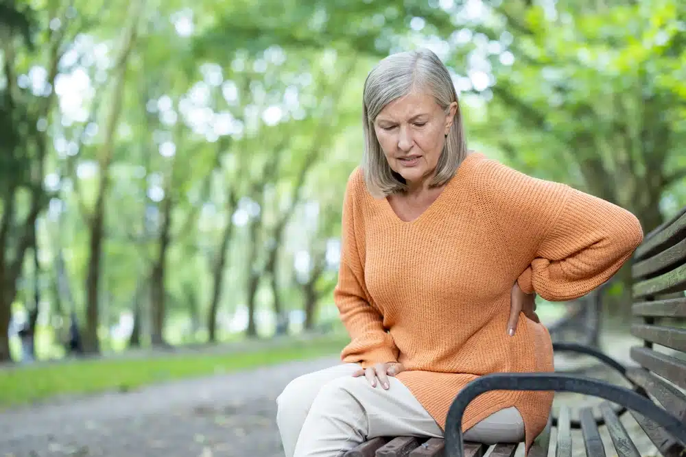 Older,Woman,With,Grey,Hair,Sitting,On,Park,Bench,Holding Woman on bench in spring with back pain